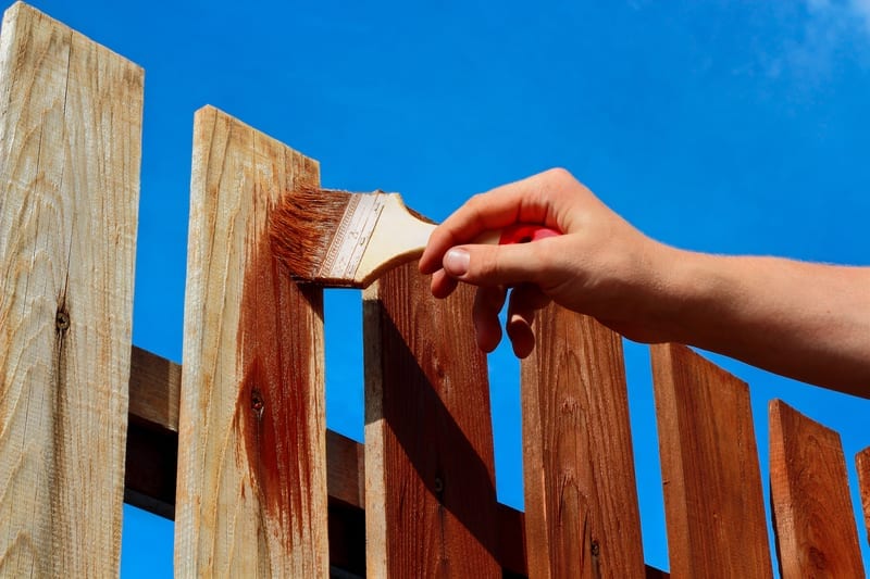 Man painting wooden fence with brown paint